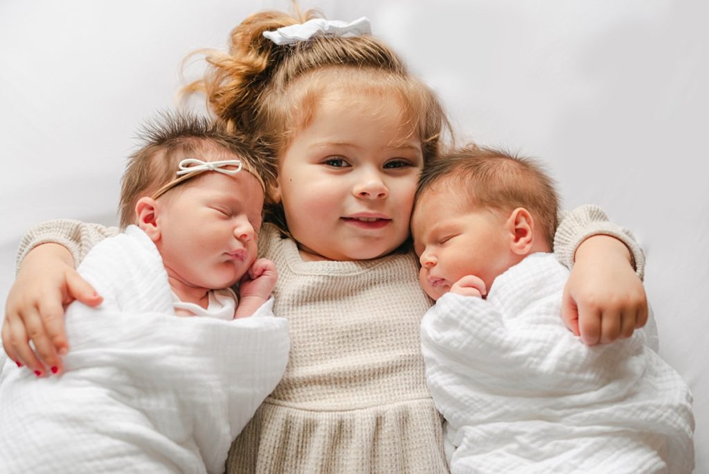 Big sister holding newborn sister and brother